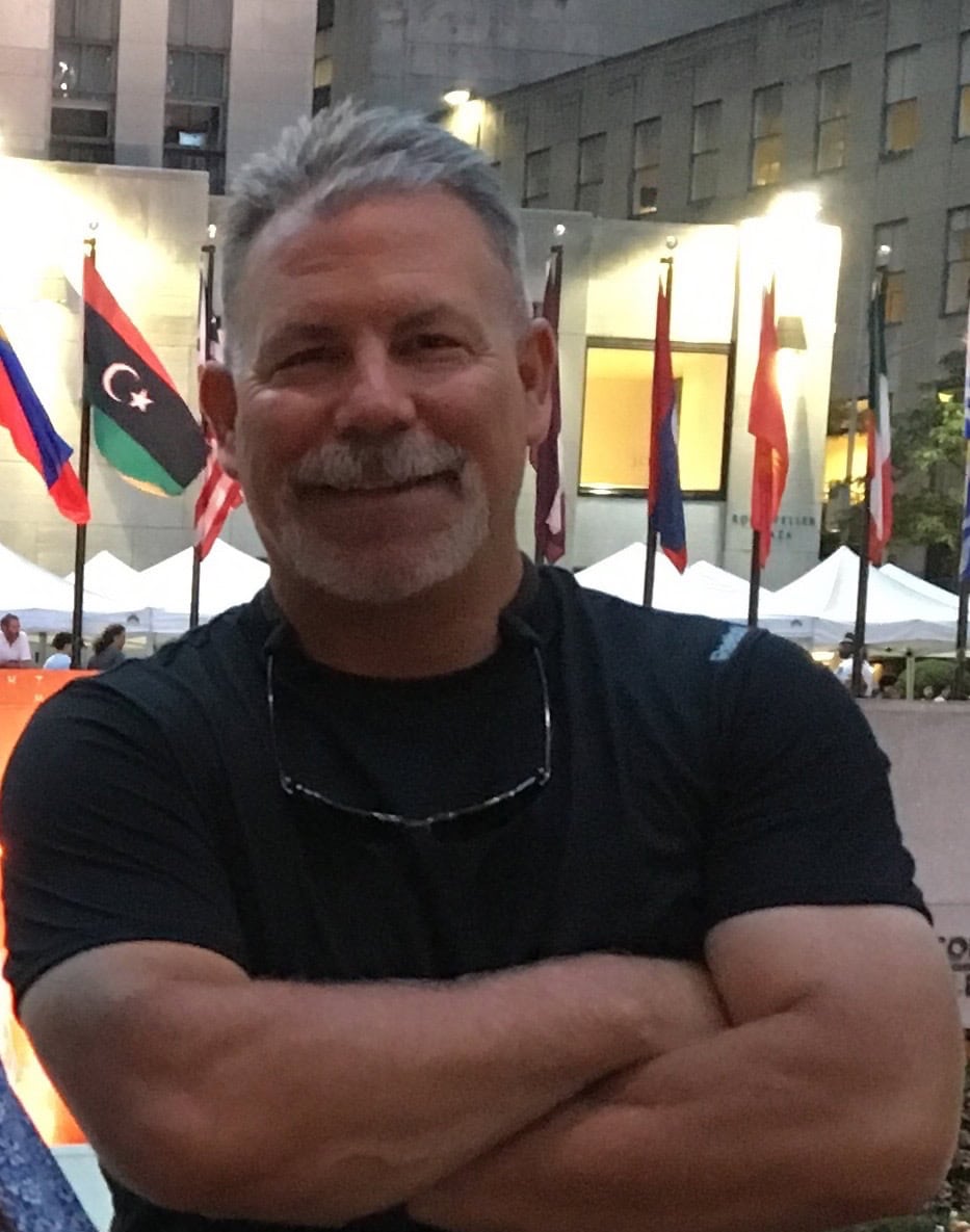Smiling man with crossed arms at international outdoor event.