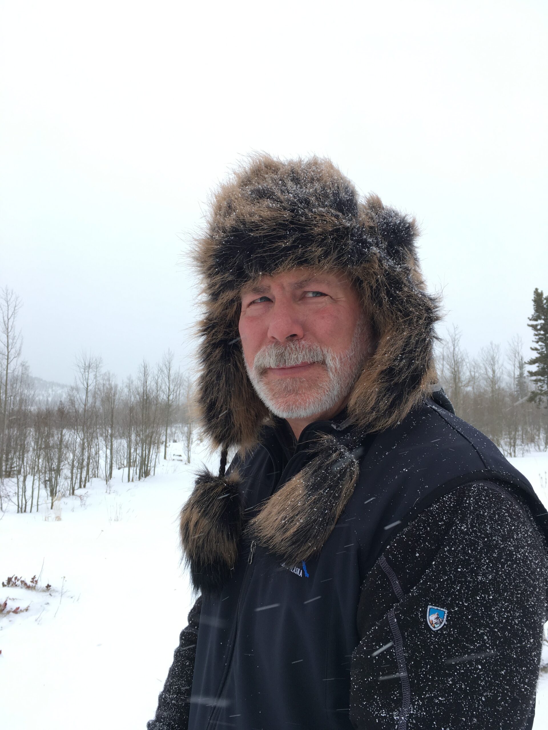 Man in winter gear with fur hat in snowy mountain landscape.